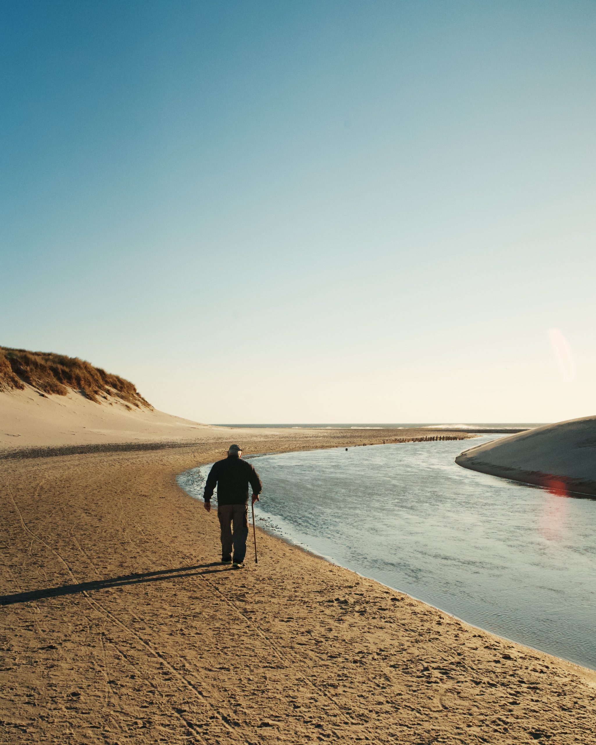 Person mayor con bantón andando a la orilla del mar
