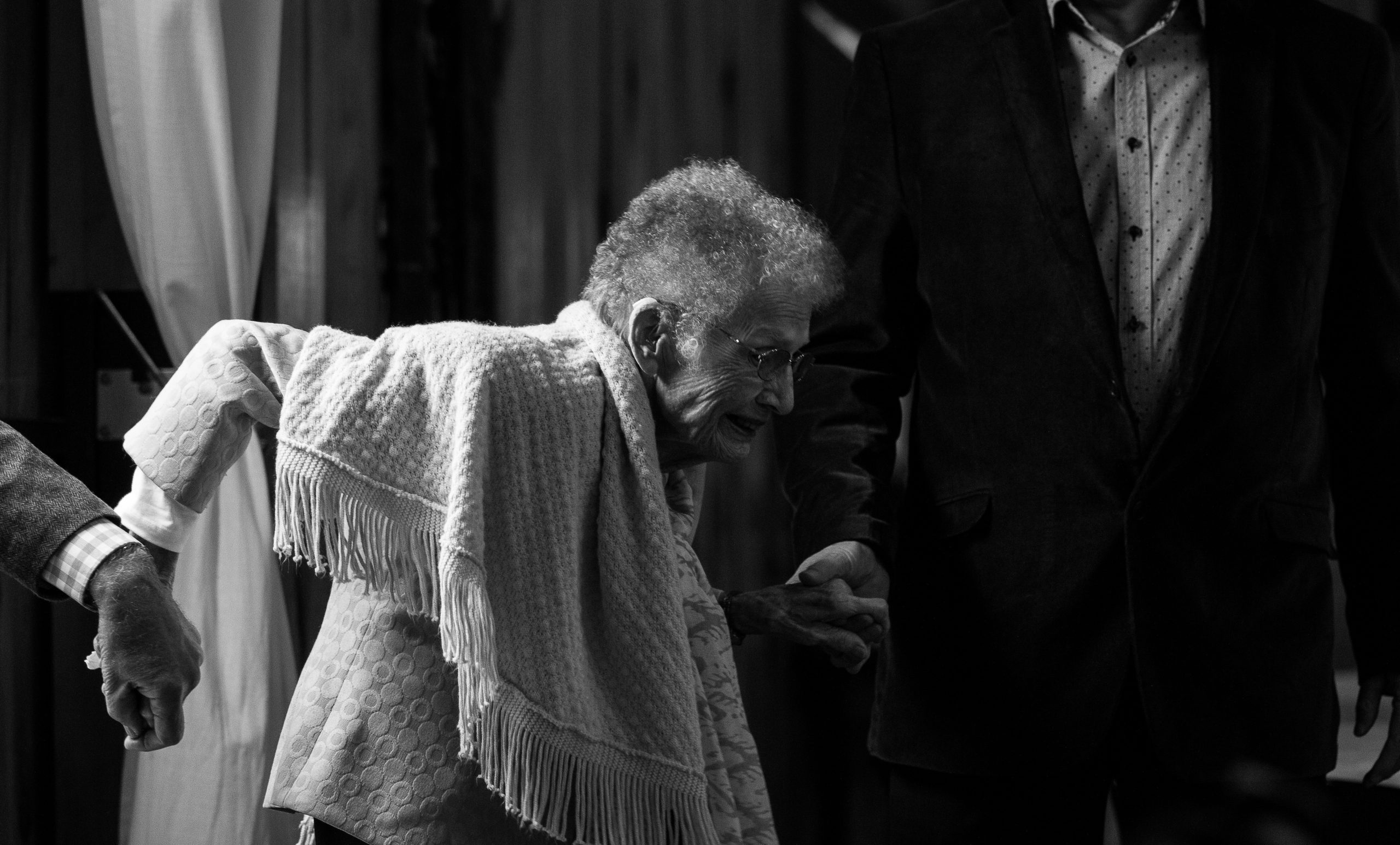 Persona mayor agarrada de la mano de dos personas que le ayudan a andar