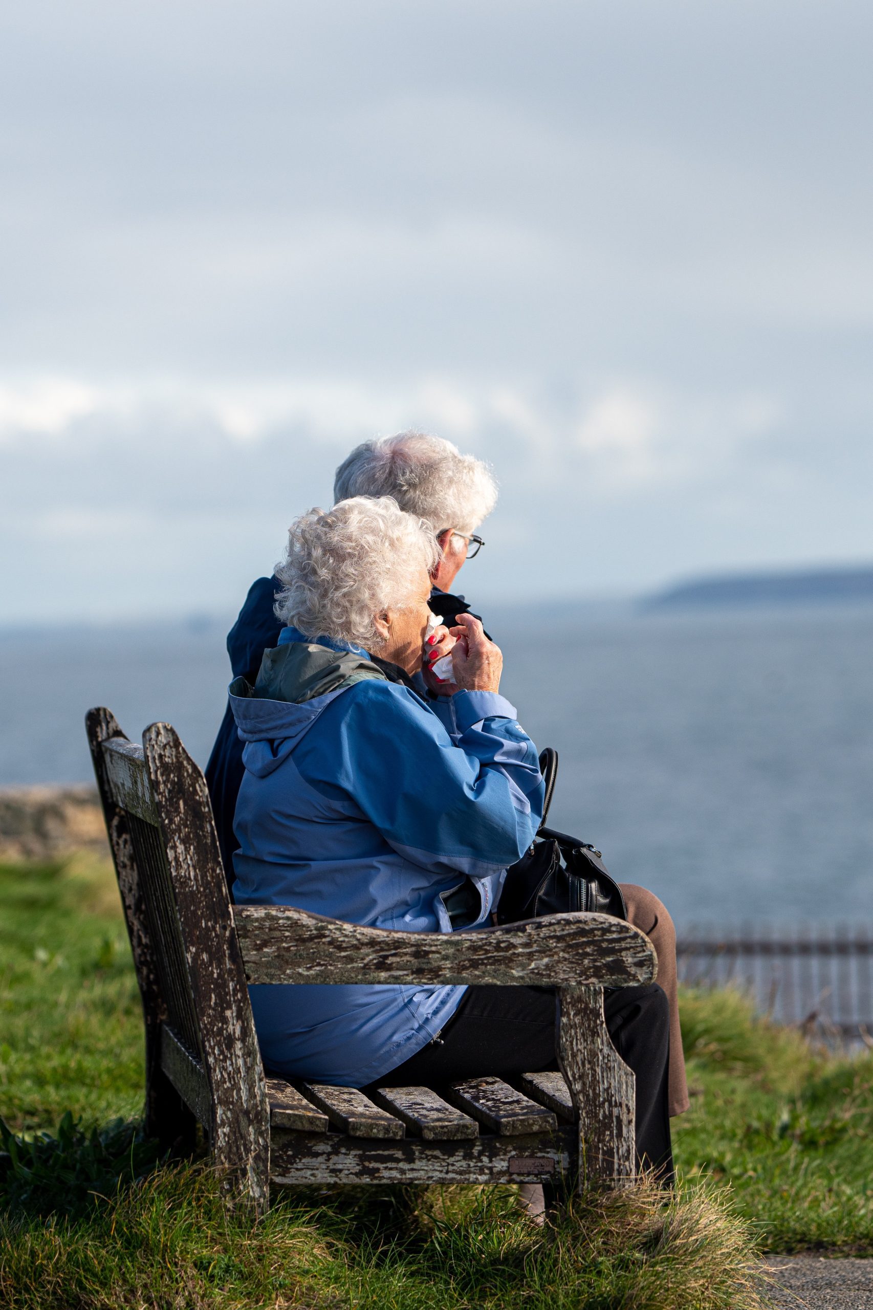 Una pareja de personas mayores sentados mirando el mar en un banco en plena naturaleza